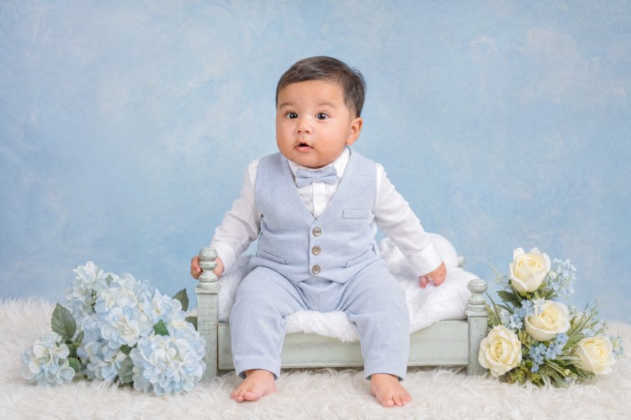 Bebé con traje azul sentado entre flores blancas