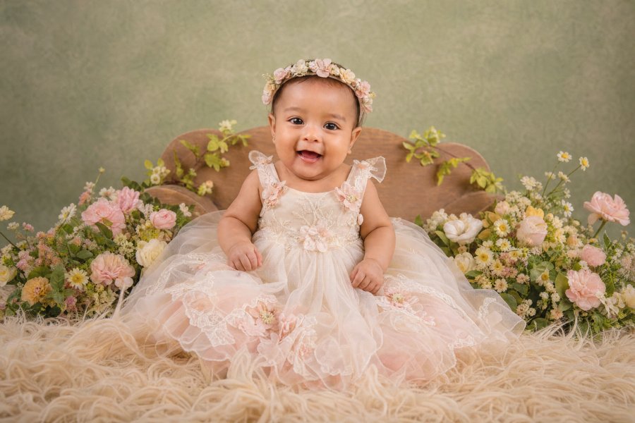 Bebé con vestido claro rodeada de flores rosadas