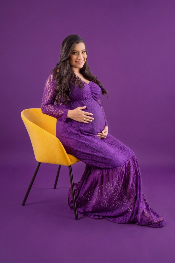 Retrato de maternidad con vestido violeta y silla amarilla