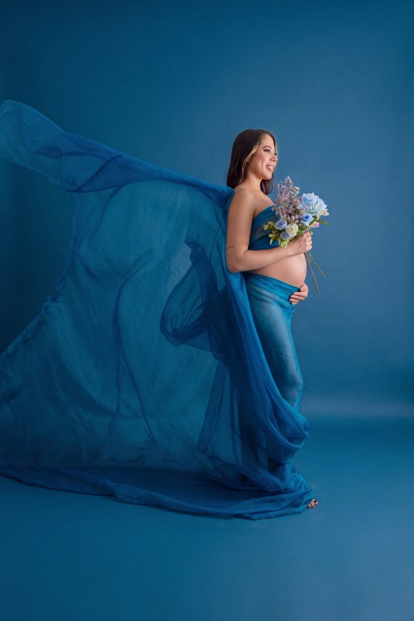 Retrato de maternidad con vestido azul, velo y ramo de flores