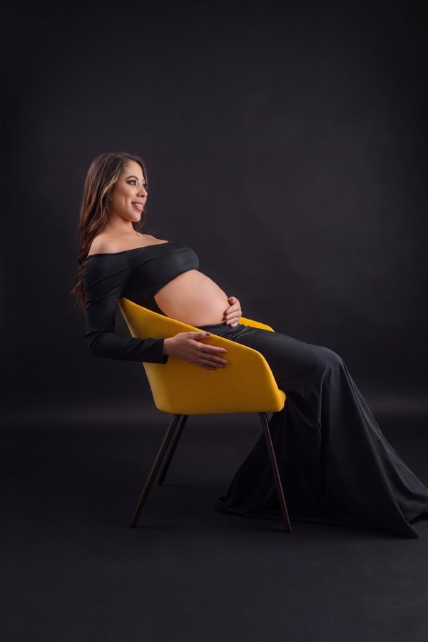Retrato de maternidad con vestido negro en silla amarilla